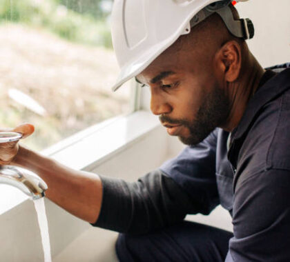 African male plumber on house call looking at bathroom tap . Young handyman trying to fix a bathroom faucet.